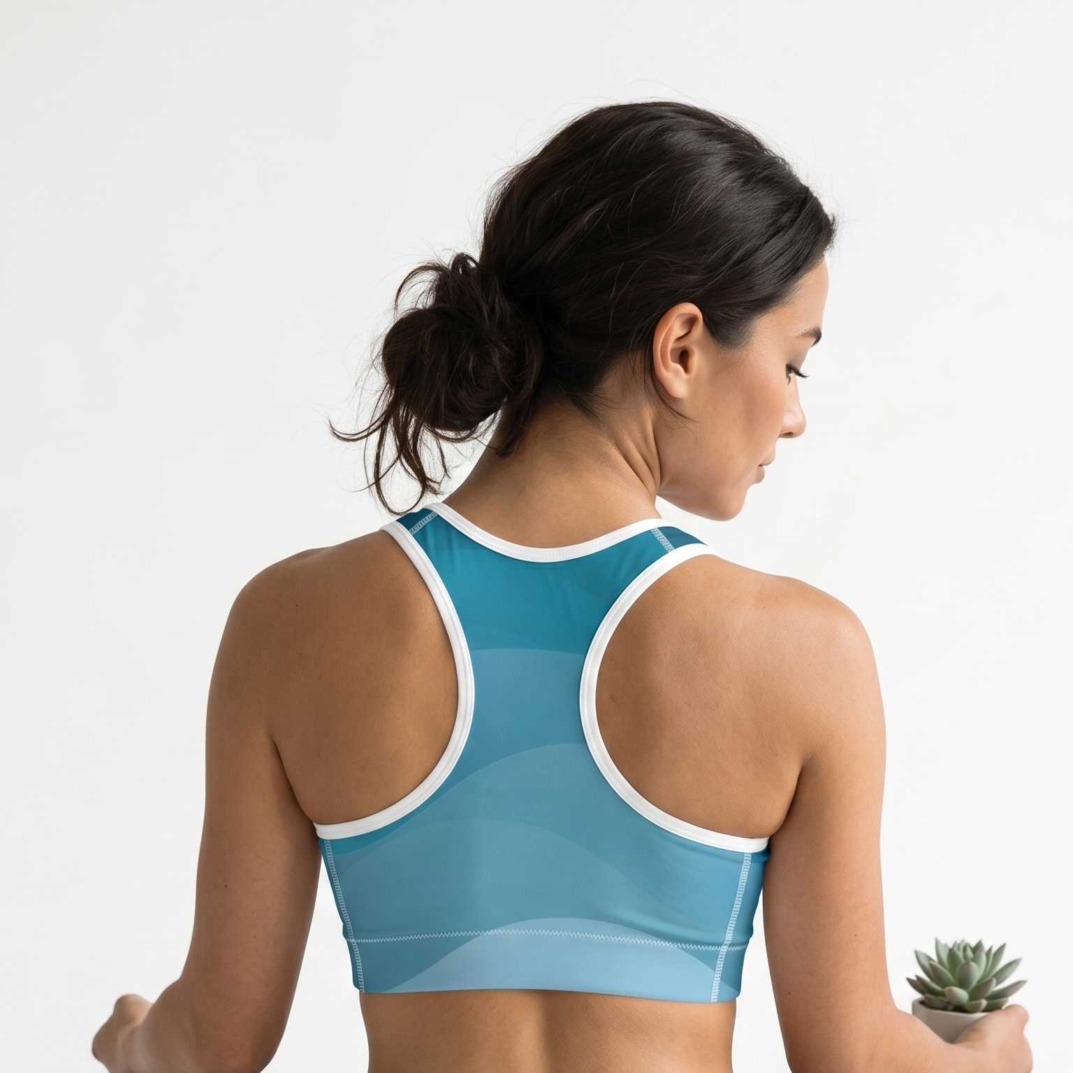 Woman in a blue sports bra and black leggings sitting on a yoga mat with a white background