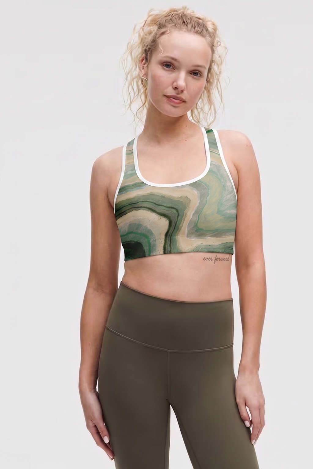 Woman wearing a green marble-patterned sports bra and olive green leggings on a white background