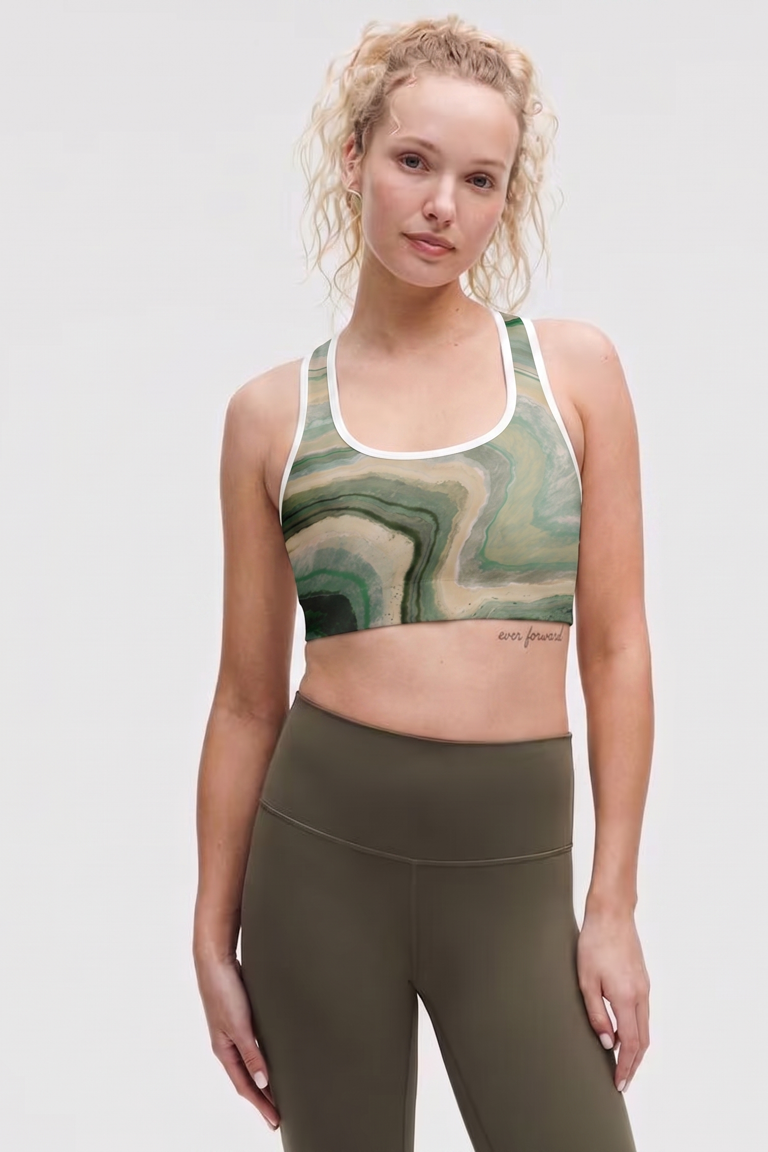 Woman wearing a green marble-patterned sports bra and olive green leggings on a white background