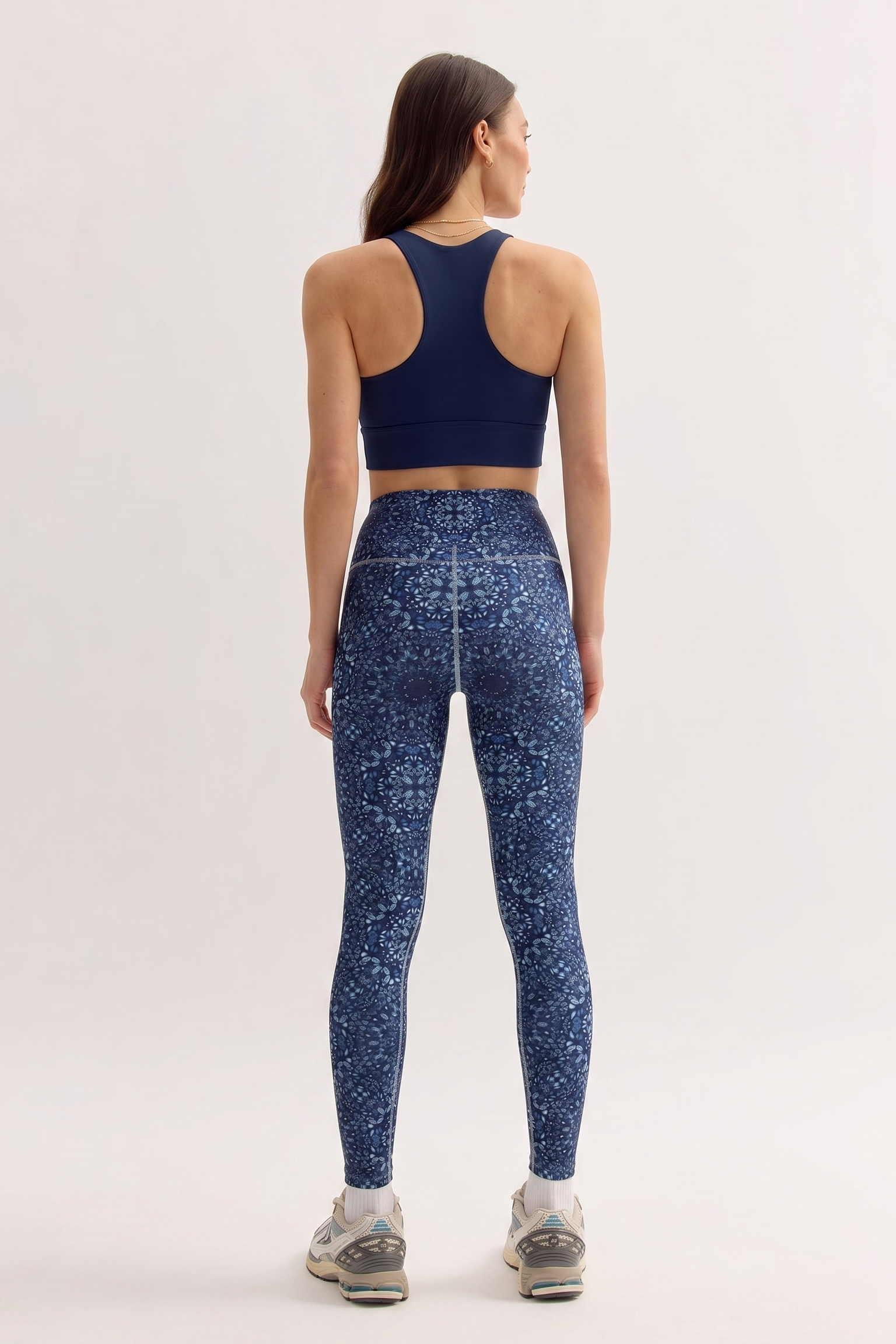 Woman wearing a navy sports bra and patterned leggings on a light background