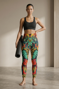 Woman holding a yoga mat wearing colorful patterned leggings and a black sports bra.