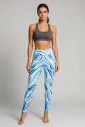 Woman wearing blue and white patterned leggings with a gray sports bra on a gray background