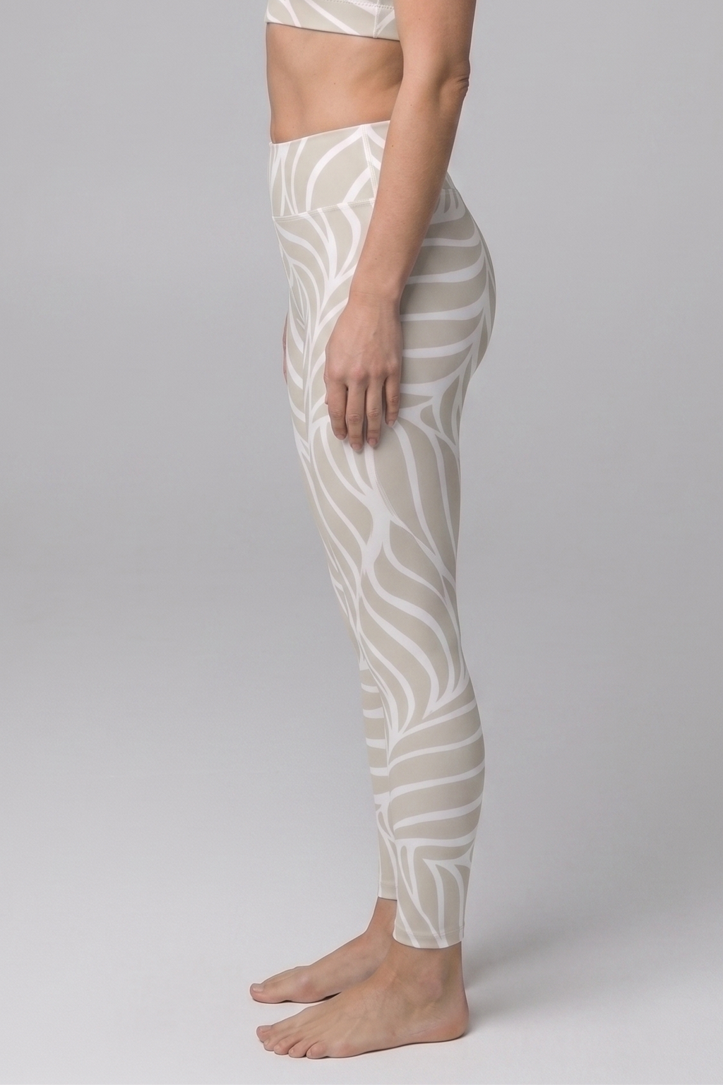 Woman wearing a white patterned sports bra and leggings on a gray background