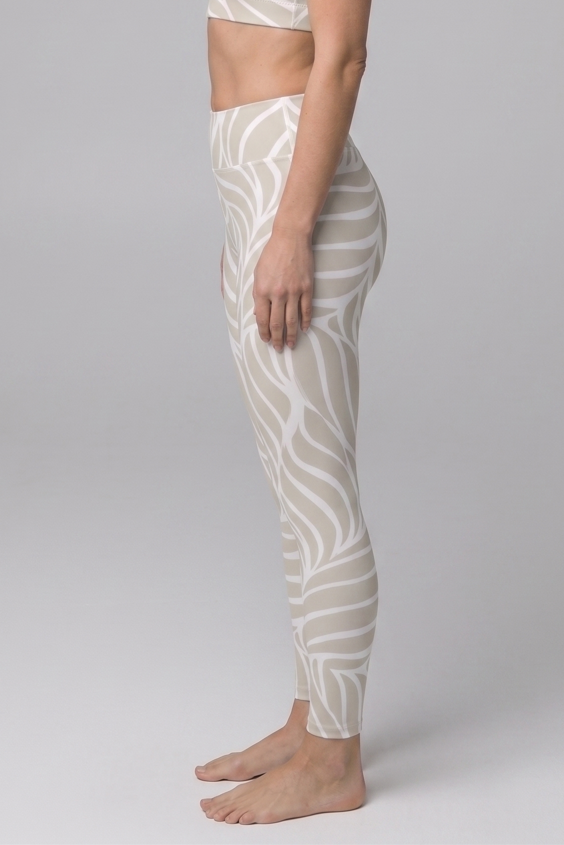 Woman wearing a white patterned sports bra and leggings on a gray background