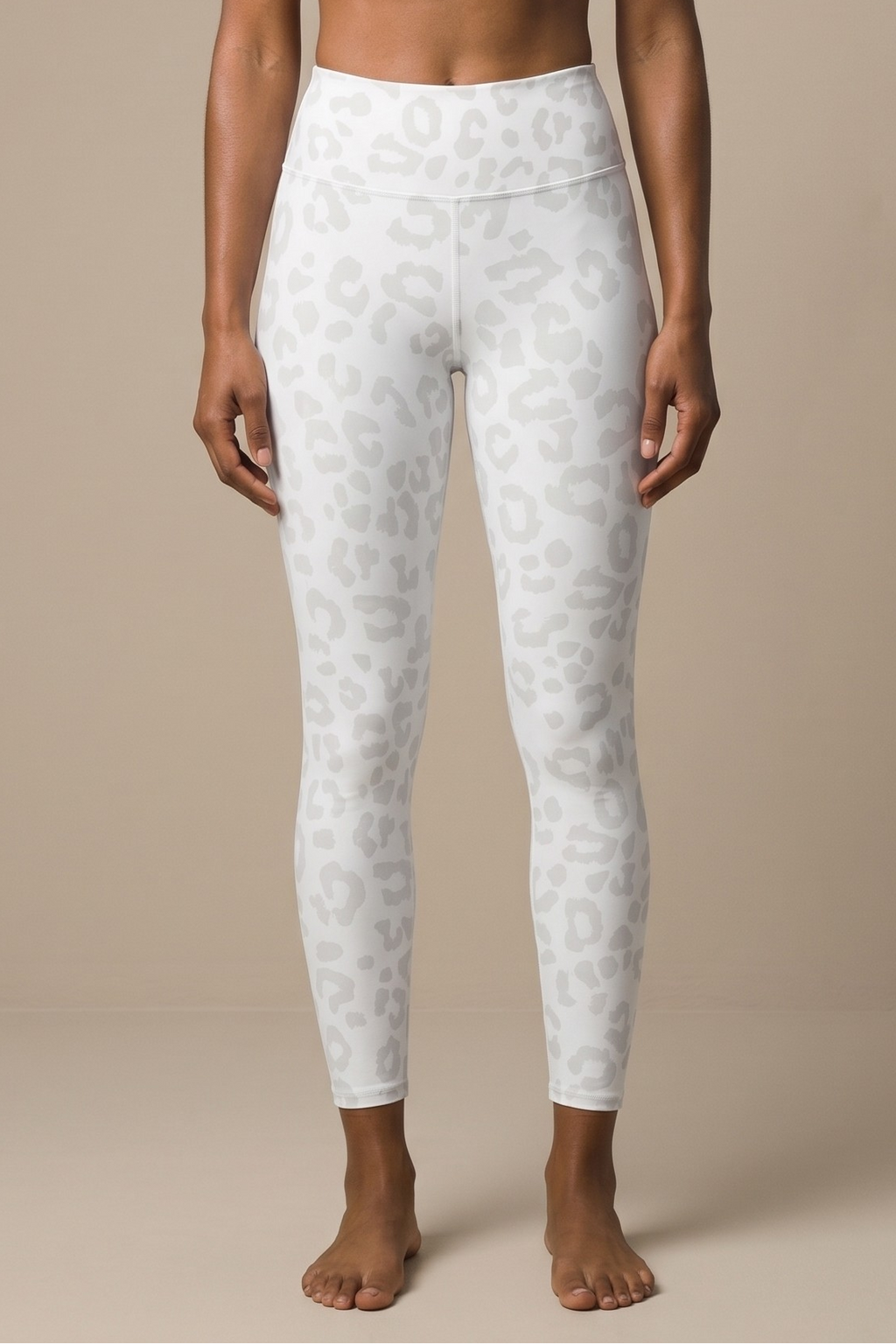 Woman wearing a white sports bra and leggings on a beige background