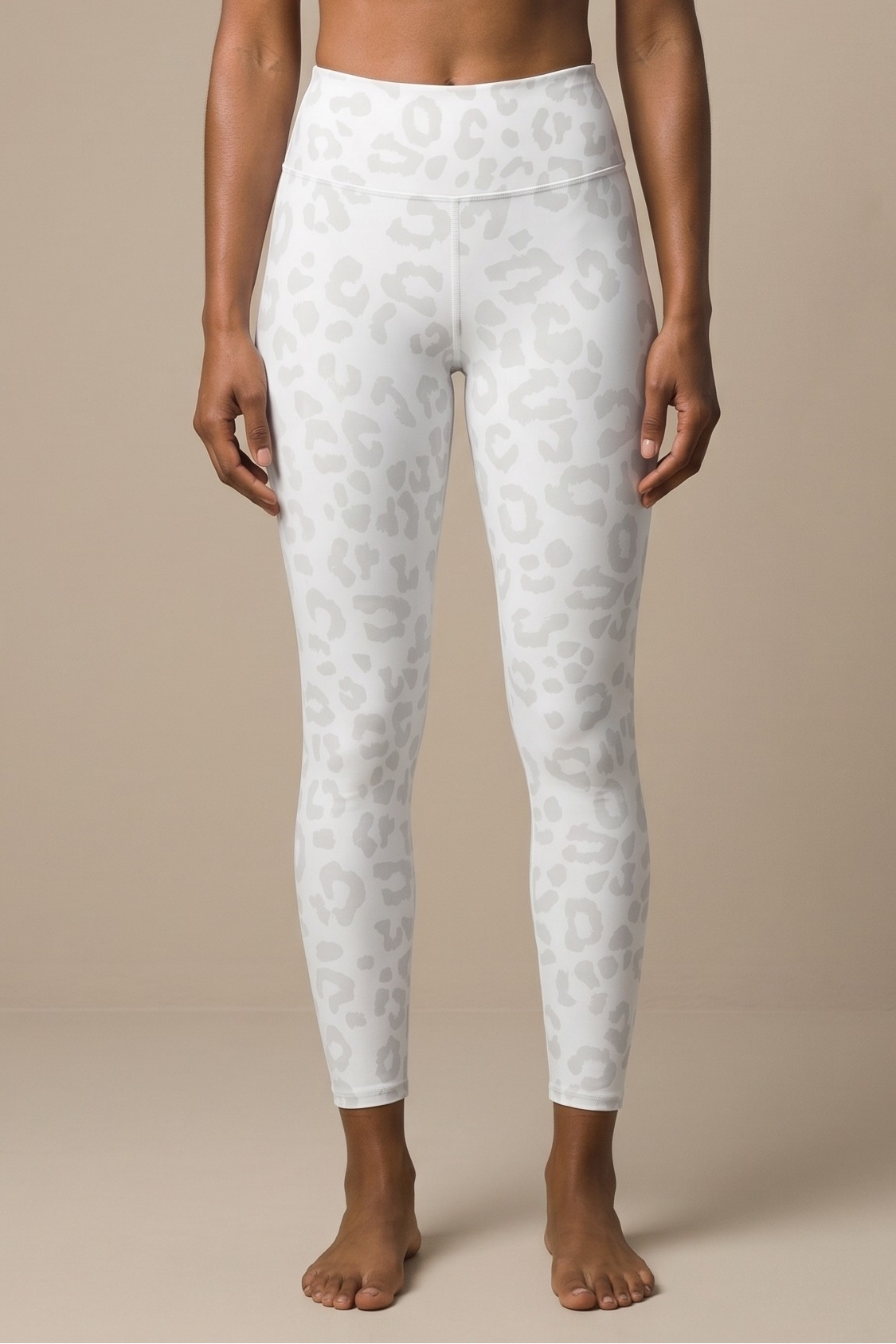 Woman wearing a white sports bra and leggings on a beige background