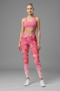 Woman wearing pink sports bra and leggings with floral pattern on a gray background