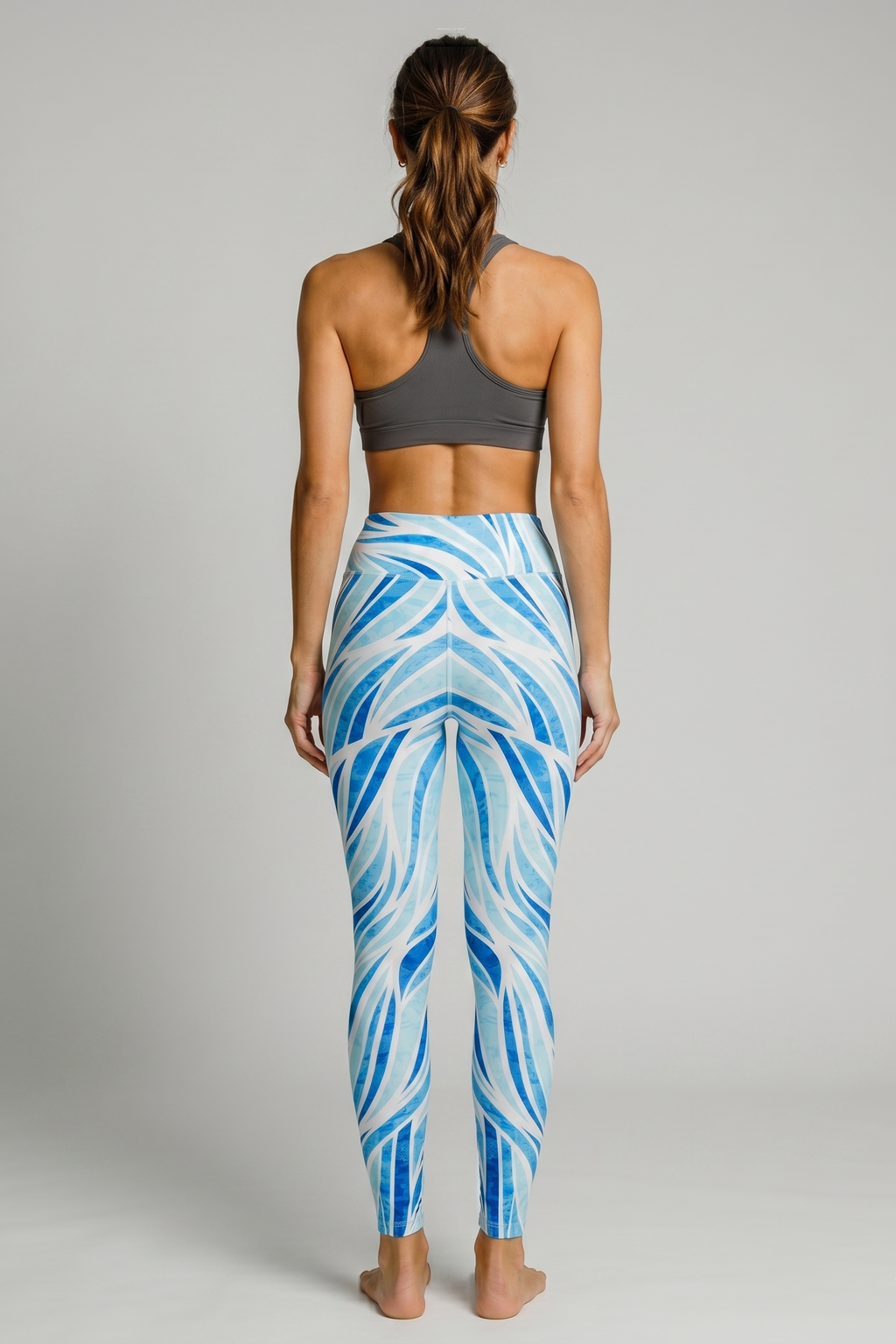 Woman wearing blue and white patterned leggings with a gray sports bra on a gray background