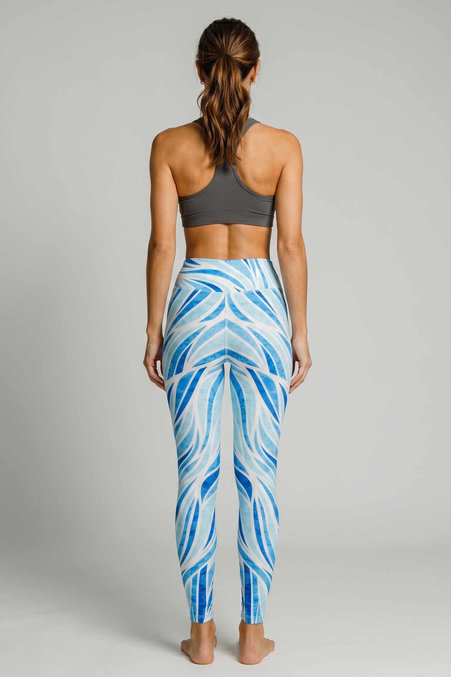 Woman wearing blue and white patterned leggings with a gray sports bra on a gray background