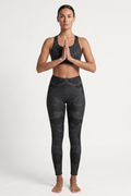 Woman wearing black patterned leggings and sports bra on a white background