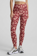 Woman wearing a white sports bra and red patterned leggings on a gray background