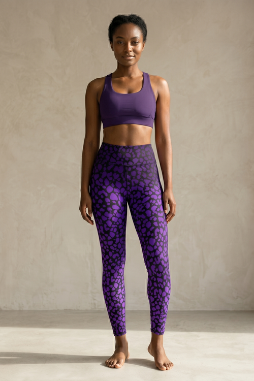 Woman wearing a purple sports bra and leggings with a pattern against a neutral background