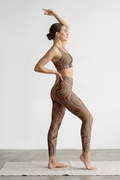 Woman in a yoga pose wearing a patterned outfit on a plain background