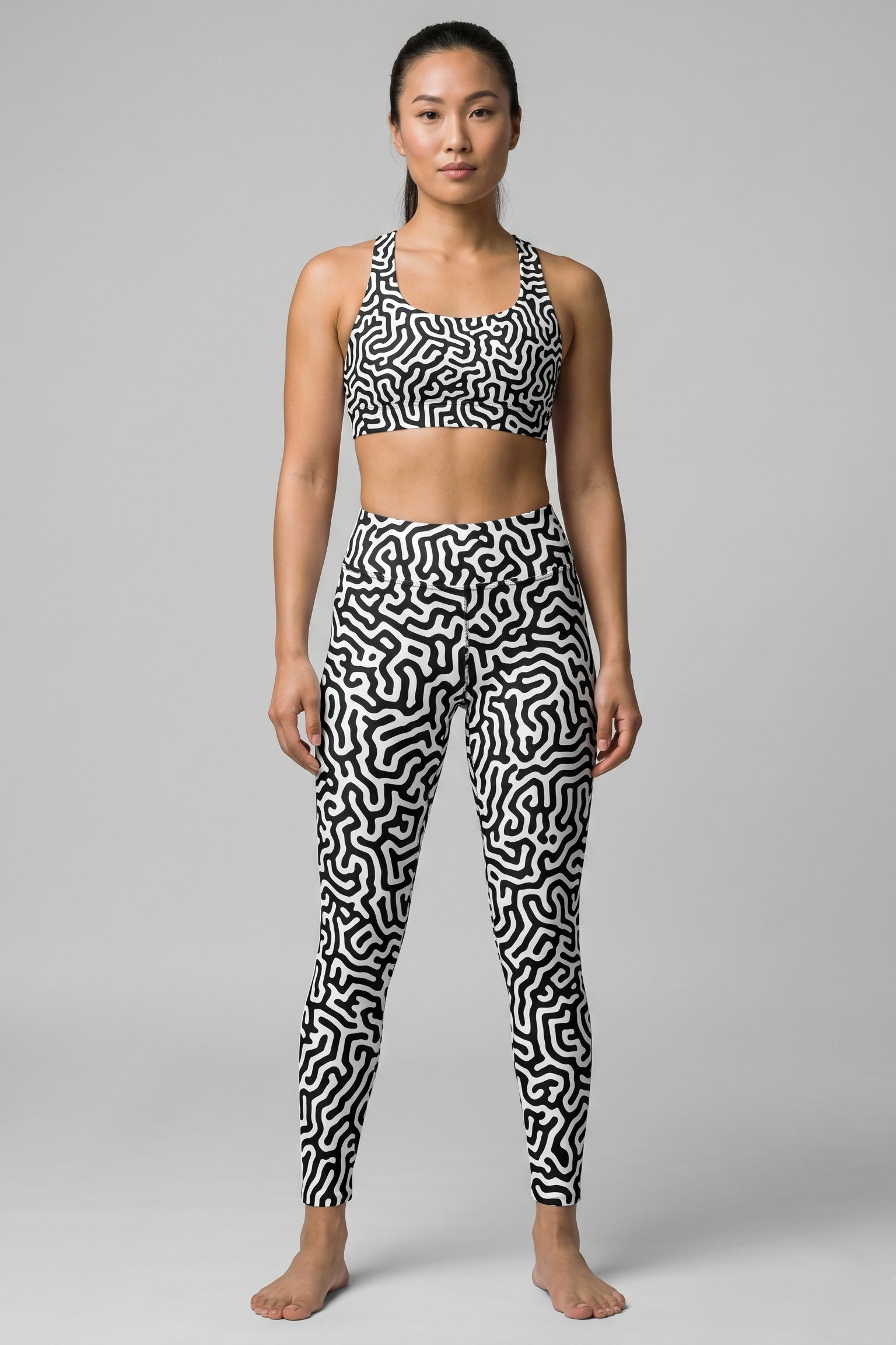 Woman wearing a black and white patterned sports bra and leggings on a gray background