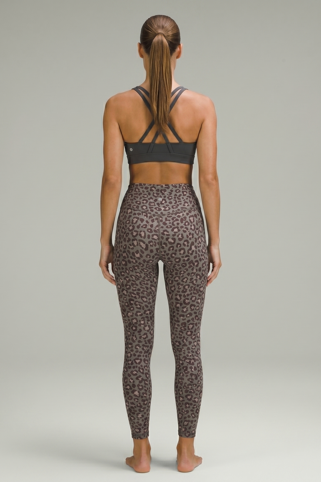 Person wearing a black sports bra and leopard print leggings on a gray background