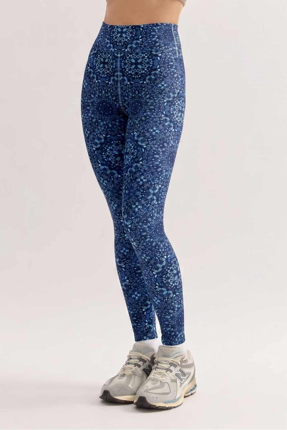 Woman wearing blue patterned leggings and a brown crop top on a white background