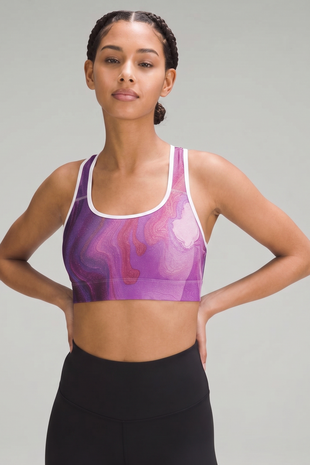 Woman wearing a purple and pink sports bra with black leggings on a gray background