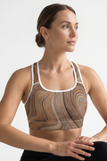 Woman wearing a patterned sports bra and black leggings on a light gray background